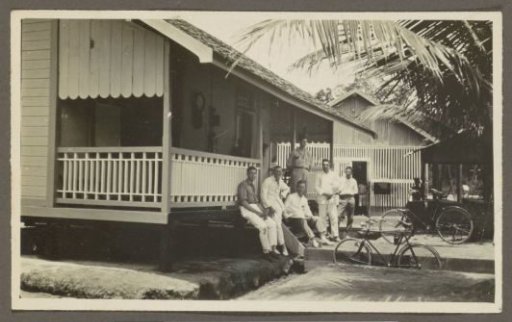 Group of men posing in front of a wooden house