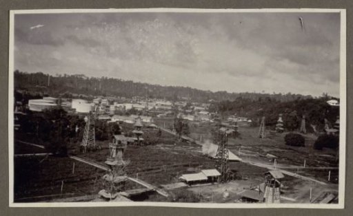 Overview of drilling towers, storage tanks and buildings amidst trees