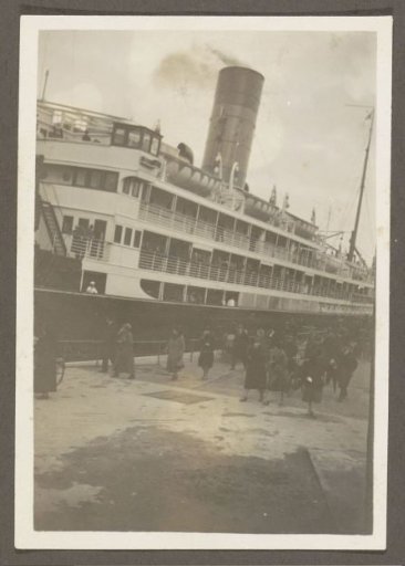 People walking along a quay next to a moored ship