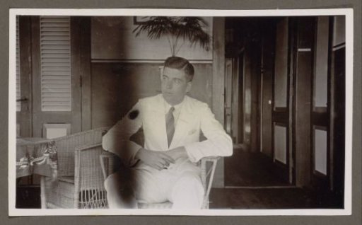 Man in a white suit sitting in a wicker armchair, hands clasped