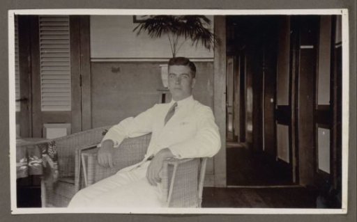 Man in a white suit sitting in a wicker armchair, arms resting