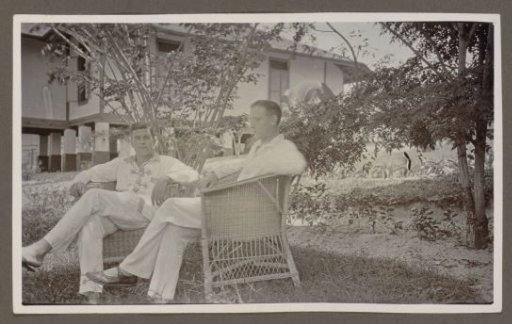 Two men in white clothing sitting in wicker armchairs in a garden