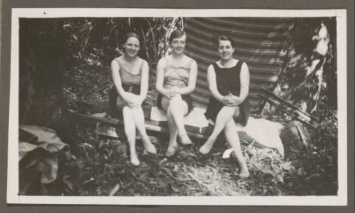Three women in swimwear sitting on a bench in a forest