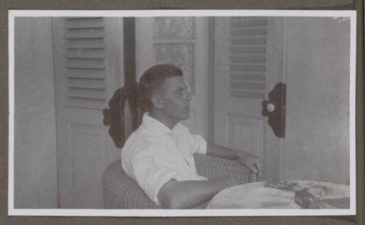 Man in a white shirt seated in a wicker chair, seen from the side