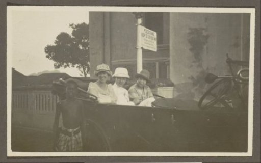 Three people sitting on the back seat of a car, a boy in front