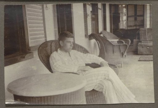 Man in pajamas sitting in a wicker chair on a veranda