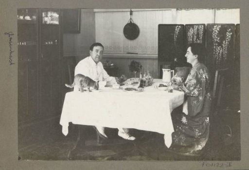 Eiso Bergsma in tropical clothing and Gerda Bergsma in a long dress seated at a dining table in a residence in Sumatra, the cat on the table