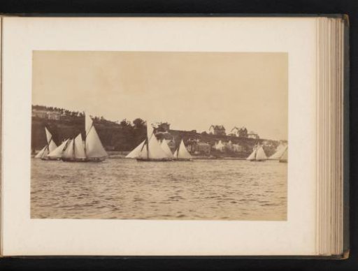 Various sailing ships afloat with buildings in the background