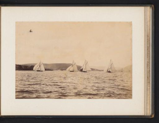 Various sailing ships afloat with a hilly landscape in the background