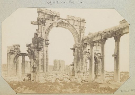 Remains of buildings including an arch in Palmyra (Syria), with a photographer at work in the foreground left