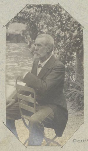 Portrait of a man with a beard, sitting backwards on a chair outdoors, probably in France