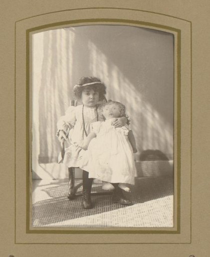 Portrait of a child seated on a chair with a doll on her lap