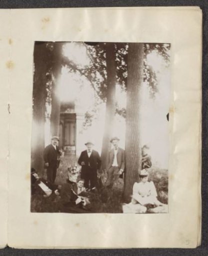 Men, women and a child posing by trees in front of a house