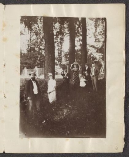 Men, women and a child posing by trees
