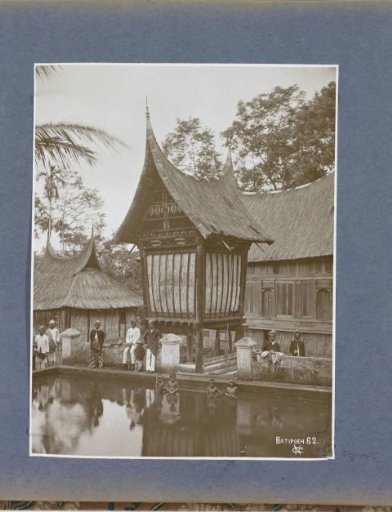 Men posing in front of padi barns in Batipoeh on Sumatra with bathing boys in the foreground