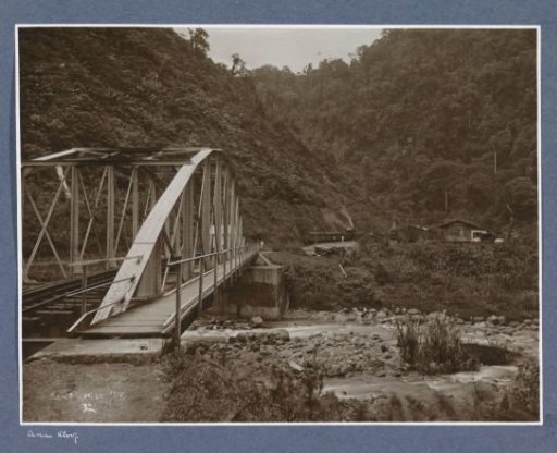Railway and pedestrian bridge at Kamp Tengah on Sumatra with a train at a station in the background
