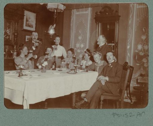 Group portrait of a company at a table where some raise their glasses, with Christiaan Otto Roelofs at the back left