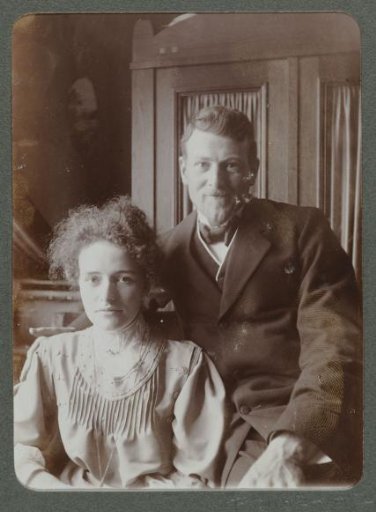Portrait of a man and woman, sitting in front of a cabinet
