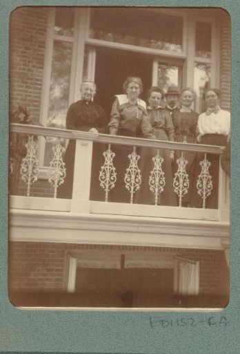 Group portrait of a man and five women in front of French doors leading to a balcony