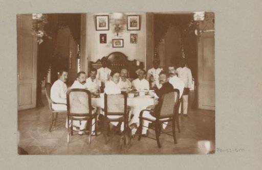 Group of European men at a table and Indonesian servants standing behind them