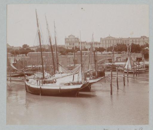 View of sailing boats in a harbor in France with a large building in the background