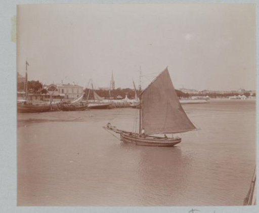 Sailing boats in a harbor in France with a church tower in the background