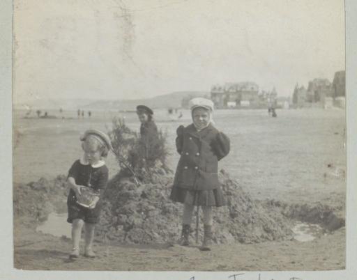 Three children playing at a sand heap on the beach, probably in Italy or France