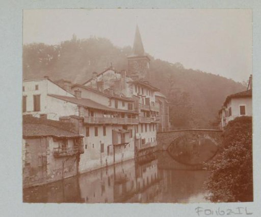 View of a village on a river with houses, a church and a bridge, probably in France