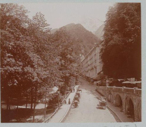 Sloping street with carriages, passers-by and buildings, probably in France