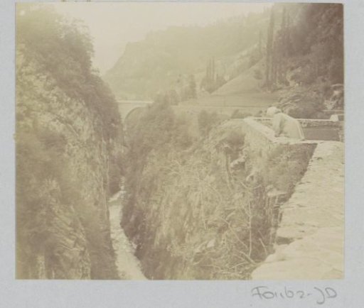 Woman looking into a gorge with a stream and a bridge, probably in the Pyrenees