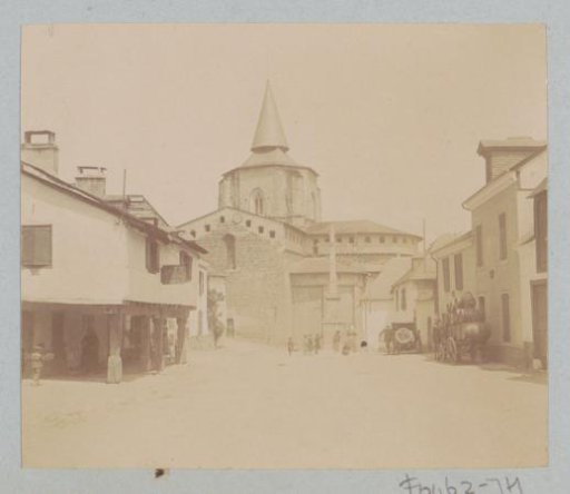 Village street with a church, a car and a cart with barrels, probably in the Pyrenees
