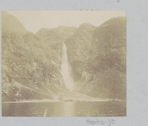 View of a mountain wall with a waterfall and a lake, probably in the Pyrenees