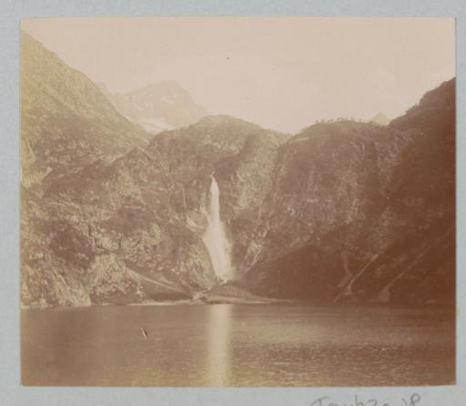 View of a mountain wall with a waterfall and a lake, probably in the Pyrenees