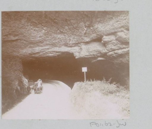 Man and a woman by a car in front of a rock tunnel, probably in the Pyrenees