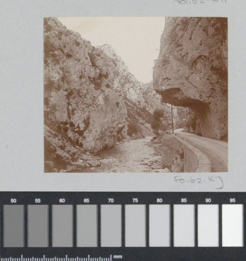Road and a stream through a partly carved-out mountain gorge, probably in the Pyrenees