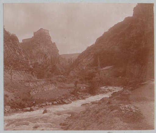 Mountain landscape with a stream and a castle on a rock, probably in the Pyrenees