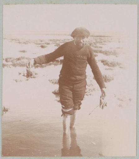Man wading through water with two dead birds in his hand during a hunting party, probably near Arcachon