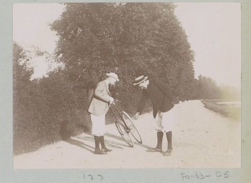 Two men bent over a bicycle on a road at Pontoise