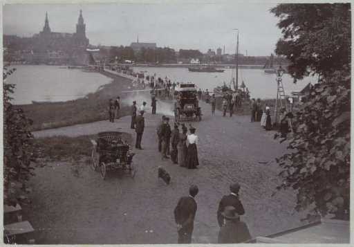 Participants in the Paris-Amsterdam race passing a pontoon bridge at Nijmegen in their automobiles, watched by the public