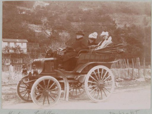 Two women and a man in an automobile on a road between Menton and Castillon