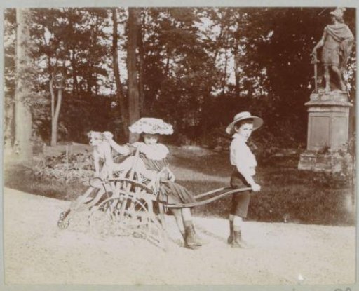 Boy, girl, dog and toy cart in a garden with a statue, probably in France