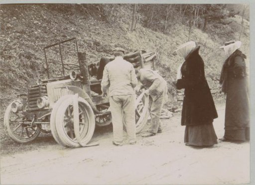 Group watching a car tire change, probably in the French Alps