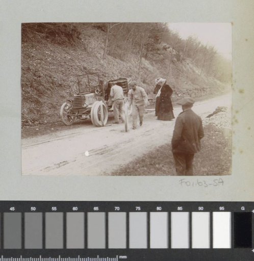 Group watching a car tire change, probably in the French Alps