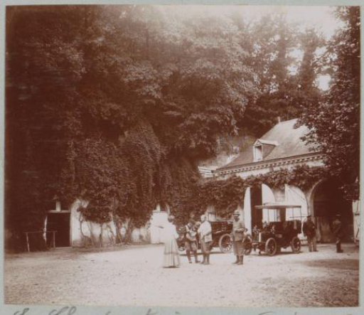 Group with two automobiles on a courtyard (designated 'La Charpenterie'), presumably at a country house or castle in France