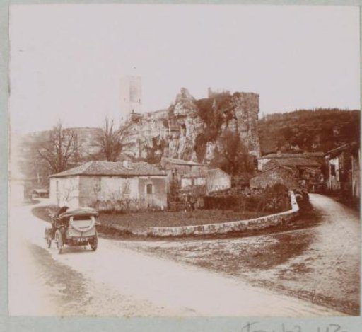 Automobile on a country road near a village with a tower, possibly in the Dordogne