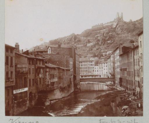 View of Vienne with houses along a river and (top right) the ruins of the Château de La Batie