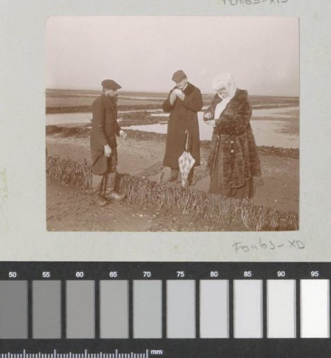 Two men and a woman, possibly tasting something on a tidal flat in France