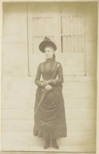 Portrait of a French girl with a hat and umbrella, standing on the steps in front of a house