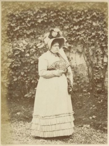 Portrait of a French woman with hat and fan, standing in a garden