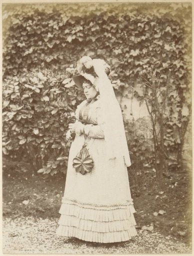 Portrait of a French woman with hat and handbag, standing in a garden